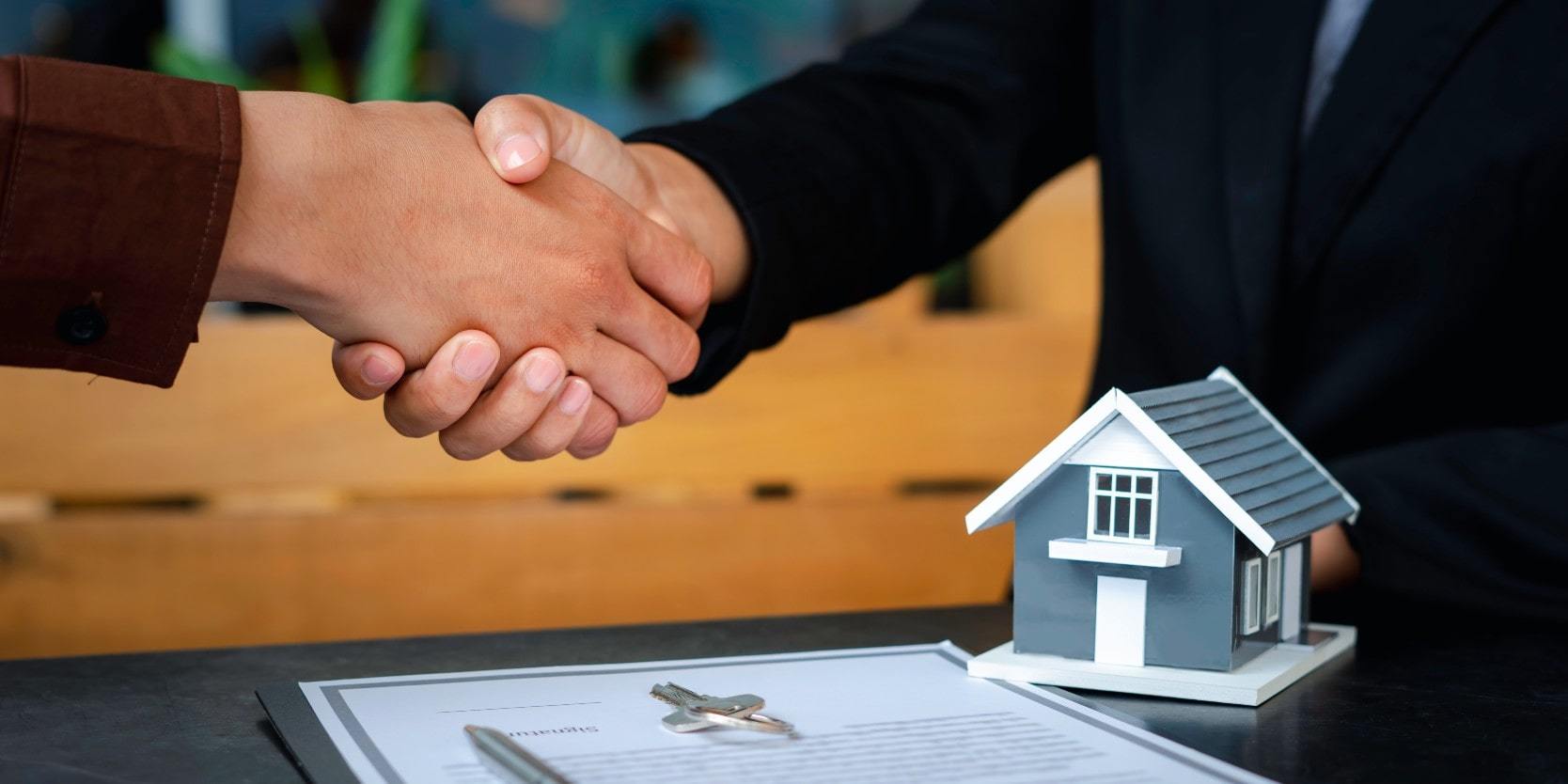 People shaking hands over a Toronto real estate assignment contract and model of a home
